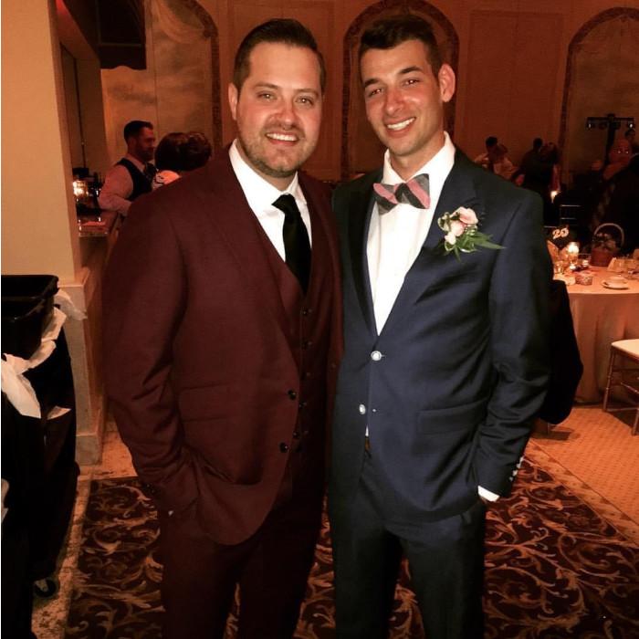 Two men wearing suits, smiling towards camera.